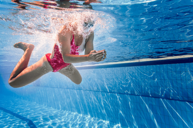 Unterwasseraufnahme eines Schwimmers in pinkem Badeanzug, der mit beiden H&auml;nden gegen die Wasseroberfl&auml;che dr&uuml;ckt.
