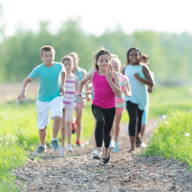 Eine Gruppe von sieben Kindern l&auml;uft fr&ouml;hlich einen Schotterweg entlang, umgeben von frischem Gr&uuml;n.