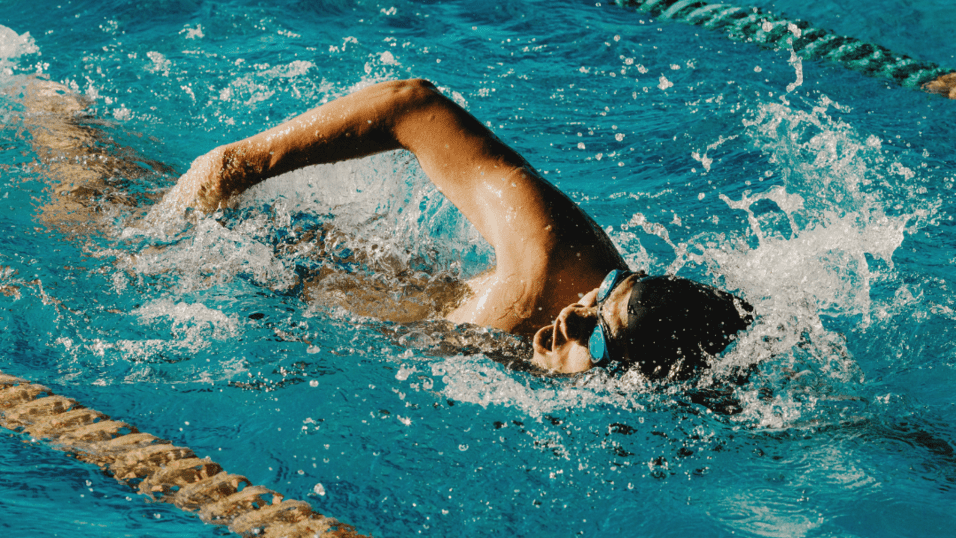Schwimmer in einer Bahn vollbringt einen Kraularmzug im blauen Wasser eines Schwimmbeckens.