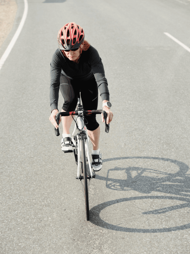 Frau in schwarzer Radbekleidung f&auml;hrt auf einem Radweg, tr&auml;gt einen roten Helm und hat eine Uhr am Handgelenk.