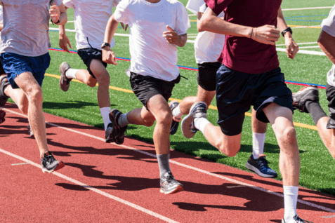 Gruppierung von L&auml;ufern in Sportswear, die auf einer roten Laufbahn sprinten, gr&uuml;ne Spielfl&auml;che im Hintergrund.