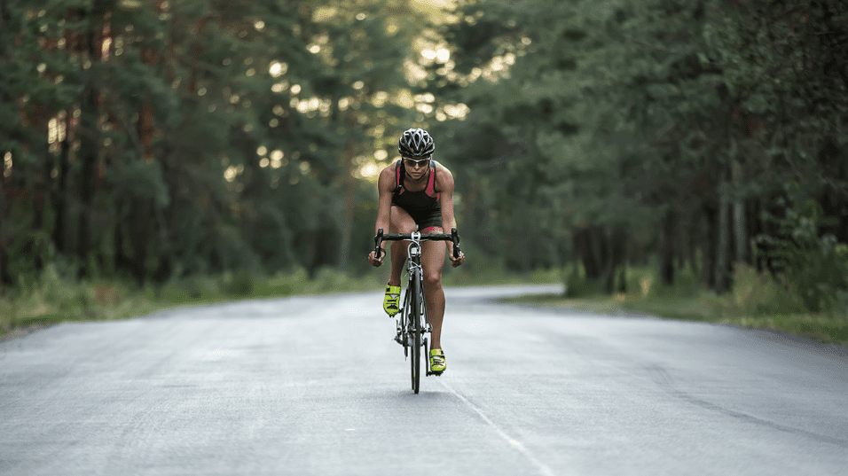 Sportler f&auml;hrt mit einem Rennrad eine verlassene Stra&szlig;e entlang, umgeben von B&auml;umen und nat&uuml;rlicher Vegetation.