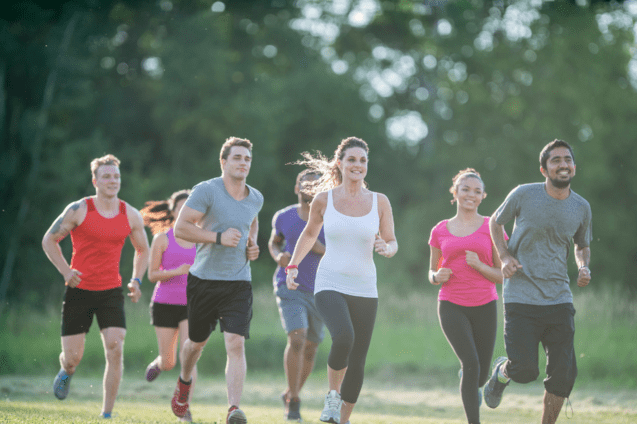 Gruppe von sechs Läufern in Sportbekleidung, die auf einer Wiese joggen, umgeben von Bäumen.