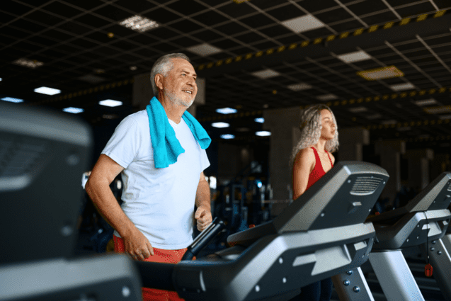 Zwei Personen joggen auf Laufb&auml;ndern in einem modernen Fitnessstudio. Der Mann tr&auml;gt ein Handtuch um den Hals.