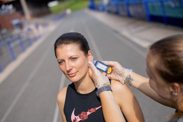 Eine Person misst die Temperatur einer Sportlerin vor einer Laufbahn.