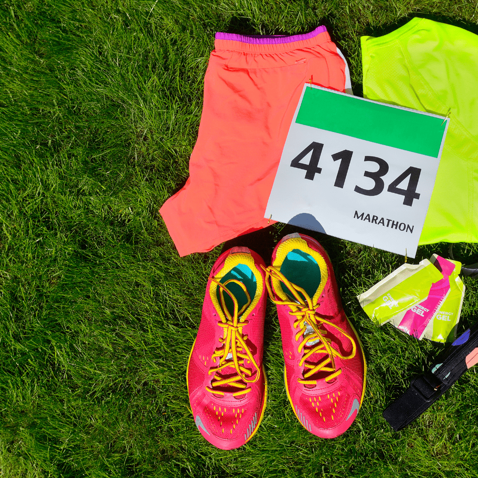Laufschuhe, Shorts, ein Sportoberteil und eine Startnummer auf grünem Gras für einen Marathon.