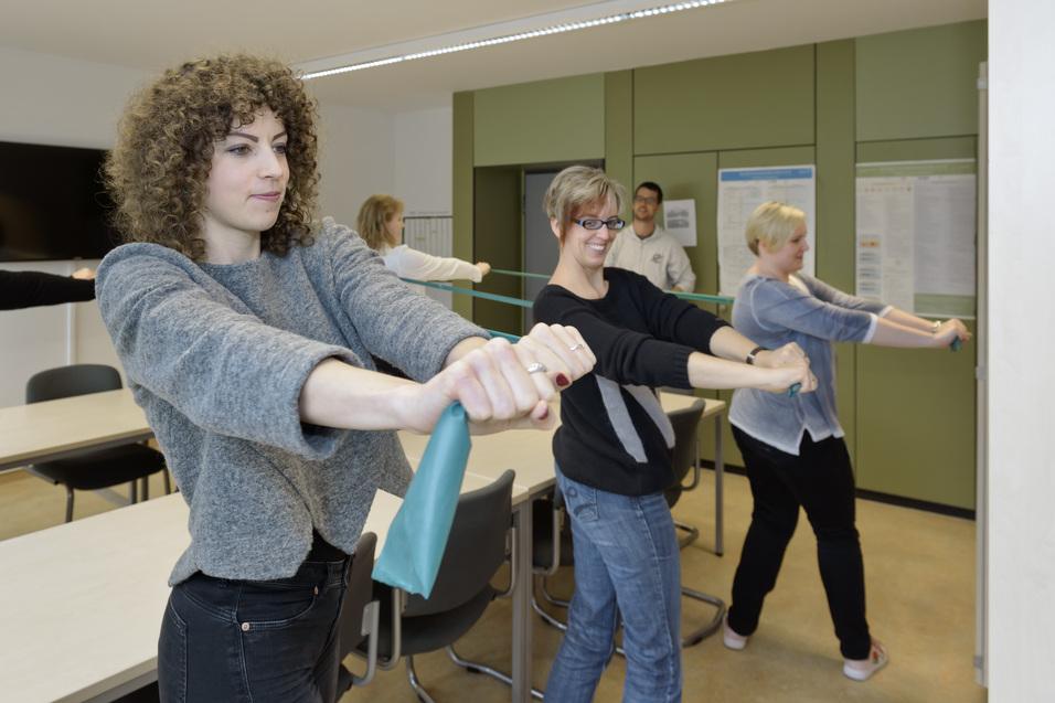 Gruppe von Frauen führt Dehnübungen mit einem elastischen Band in einem hellen Raum durch.
