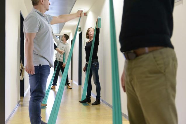 Gruppentraining mit Widerstandsbändern in einem Flur; mehrere Personen dehnen und halten die Bänder.