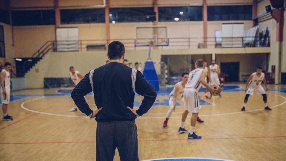 Basketballtrainer beobachtet das Training von Spielern auf dem Holzparkett eines Sportfeldes.