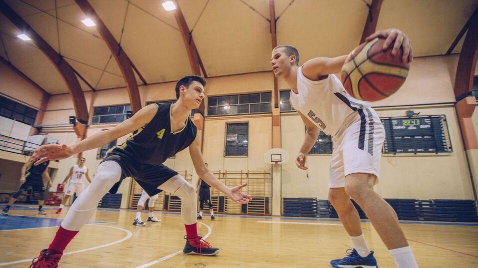Zwei Basketballspieler in Aktion auf dem Spielfeld, einer dribbelt, der andere verteidigt.