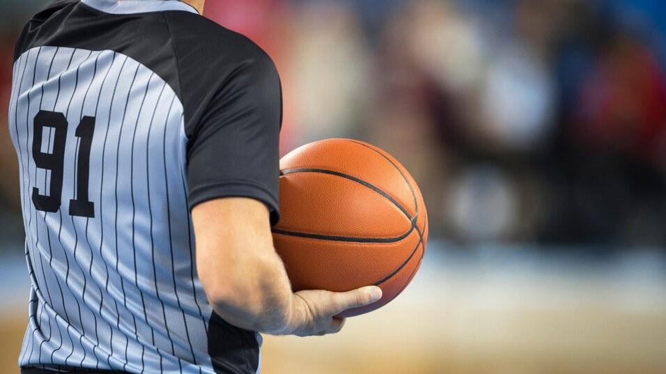 Nahaufnahme eines Basketballschiedsrichters mit einer orangefarbenen Basketball in der Hand, die Trikotnummer 91 sichtbar.