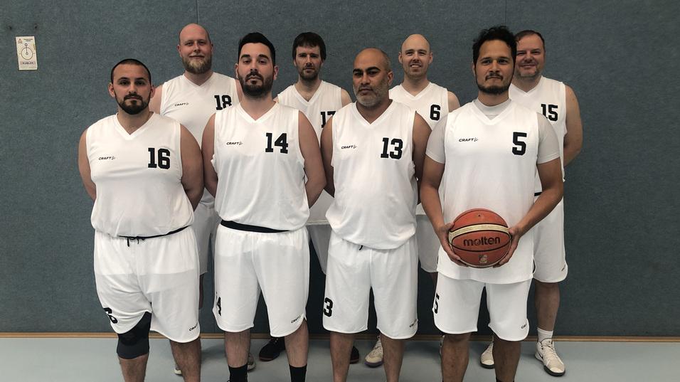 Eine Gruppe von acht Basketballspielern in wei&szlig;en Trikots steht auf einem Sportfeld, einer h&auml;lt einen Basketball in der Hand.