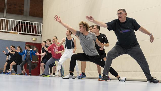 Gruppe von Sportlern in Trainingskleidung f&uuml;hrt synchron &Uuml;bungen in einer Sporthalle durch.