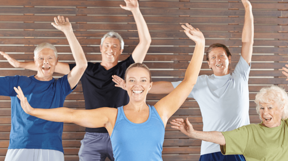 Gruppe &auml;lterer Erwachsenen macht gemeinsam &Uuml;bungen in einem Fitnesskurs mit fr&ouml;hlichen Gesichtern und gestreckten Armen.