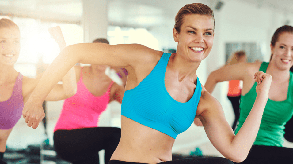 Gruppe von Frauen in Sportkleidung, die in einem Fitnessstudio eine Tanz-Workout-Übung ausführen.