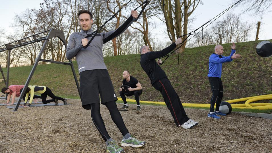 Gruppe von M&auml;nnern und Frauen beim Outdoor-Workout mit Seil- und Kettlebell-&Uuml;bungen auf Holzhackschnitzelboden.