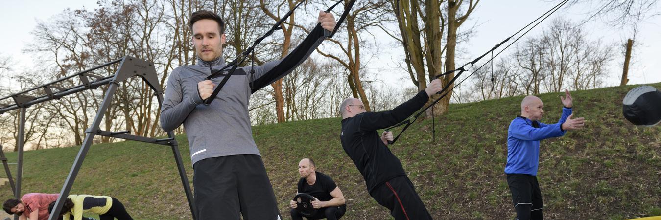 Gruppe von M&auml;nnern und Frauen beim Outdoor-Workout mit Seil- und Kettlebell-&Uuml;bungen auf Holzhackschnitzelboden.