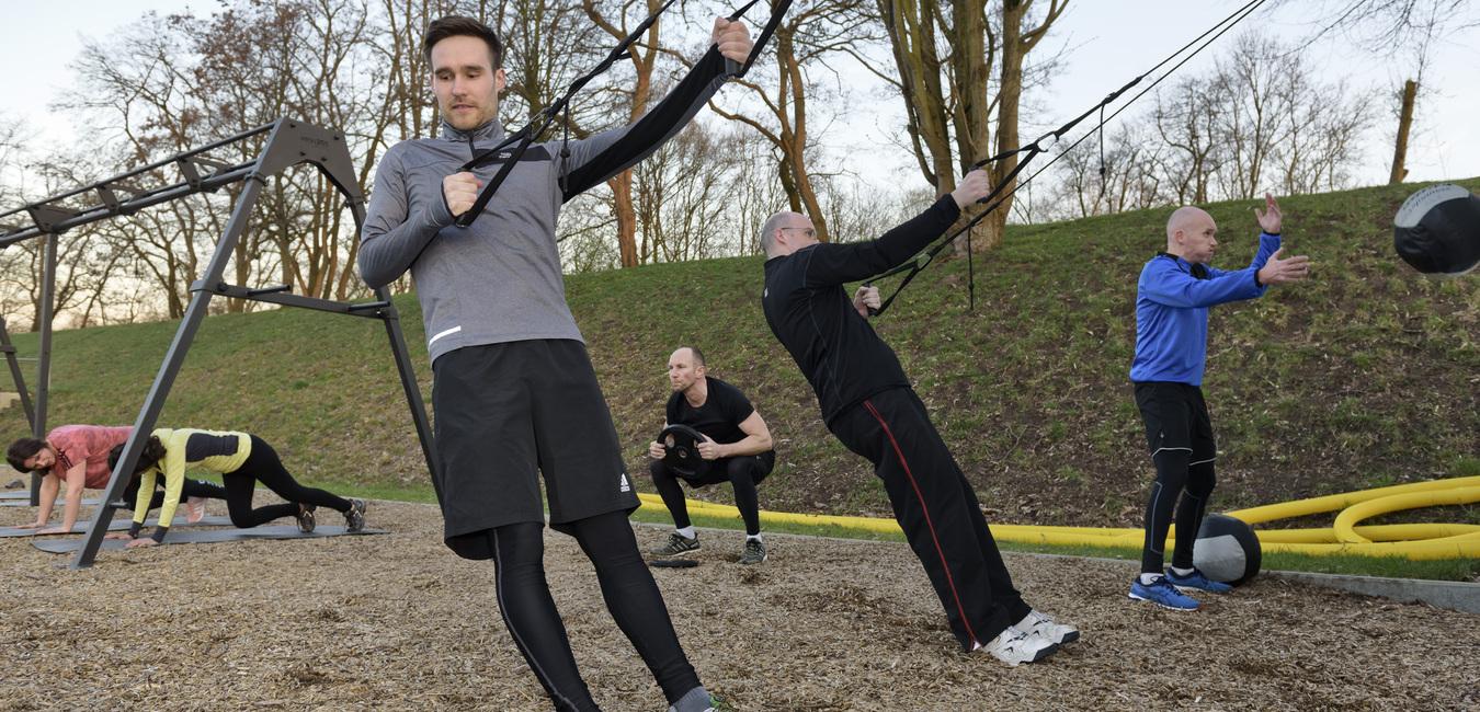 Gruppe von M&auml;nnern und Frauen beim Outdoor-Workout mit Seil- und Kettlebell-&Uuml;bungen auf Holzhackschnitzelboden.