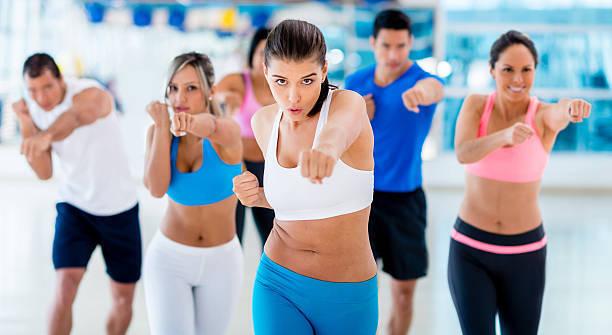 Gruppe von sechs Menschen in Sportkleidung, die synchron F&auml;uste aussto&szlig;en w&auml;hrend eines Fitnesskurses in einem Studio.