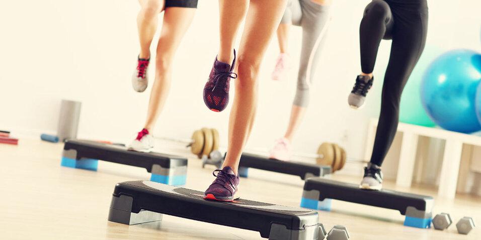Gruppentraining: Nahaufnahme von vier Menschen, die auf Step-Aerobic-Boards in einem Fitnessstudio steppen.