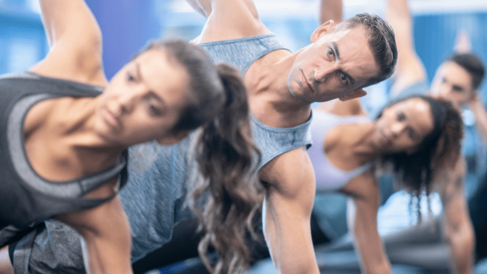 Gruppentraining mit vier Personen in Plank-Position auf einer Fitnessmatte in einem modernen Gym.