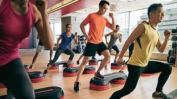 Gruppe von Menschen beim Step-Aerobic-Training auf Step-Brettern in einem modernen Fitnessstudio.