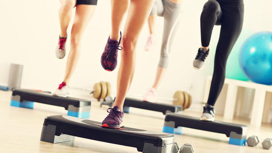 Gruppentraining: Nahaufnahme von vier Menschen, die auf Step-Aerobic-Boards in einem Fitnessstudio steppen.