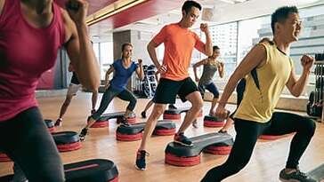 Gruppe von Menschen beim Step-Aerobic-Training auf Step-Brettern in einem modernen Fitnessstudio.