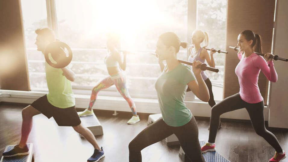 Sechs Personen absolvieren ein Krafttraining mit Gewichten in einem hellen Fitnessstudio.
