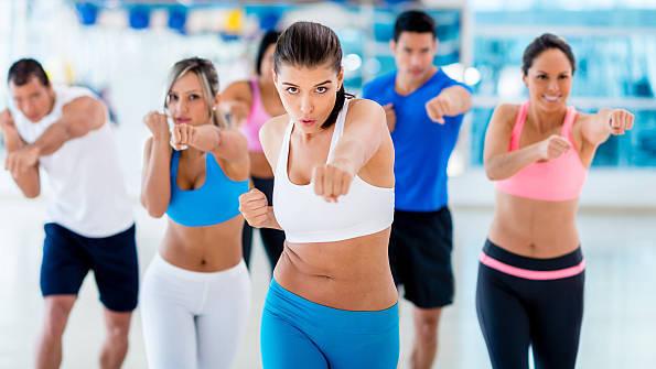 Gruppe von sechs Menschen in Sportkleidung, die synchron F&auml;uste aussto&szlig;en w&auml;hrend eines Fitnesskurses in einem Studio.