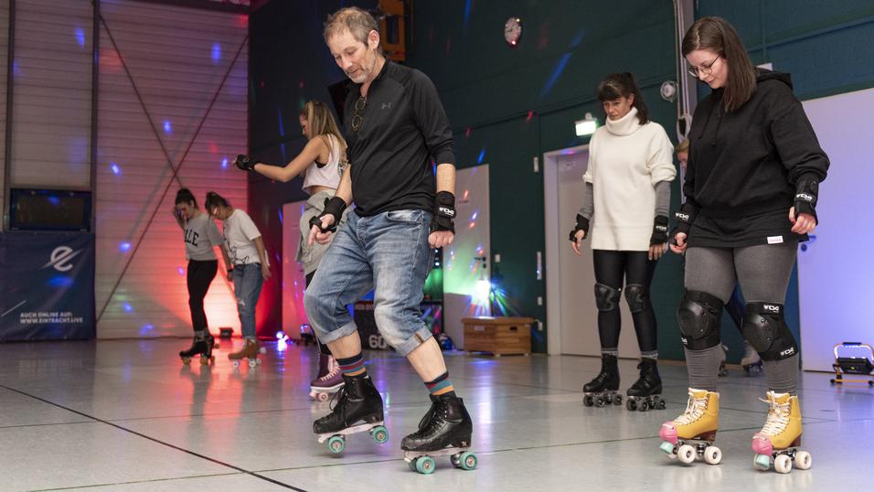 Eine Gruppe von Menschen rollt auf Rollschuhen in einer Halle mit bunten Lichtern und Musik.