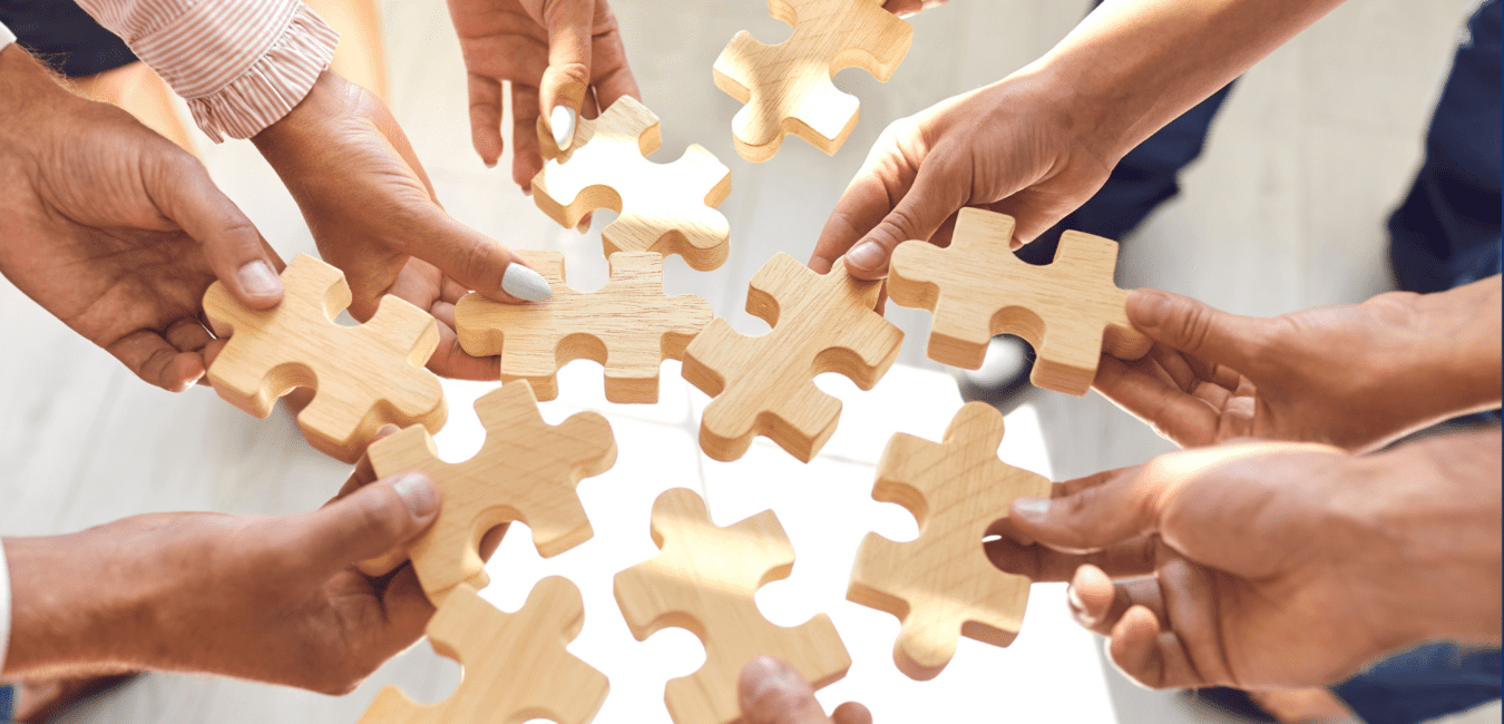 Hände mehrerer Personen halten Holz-Puzzlestücke, die sich überlappend in der Mitte gruppieren.