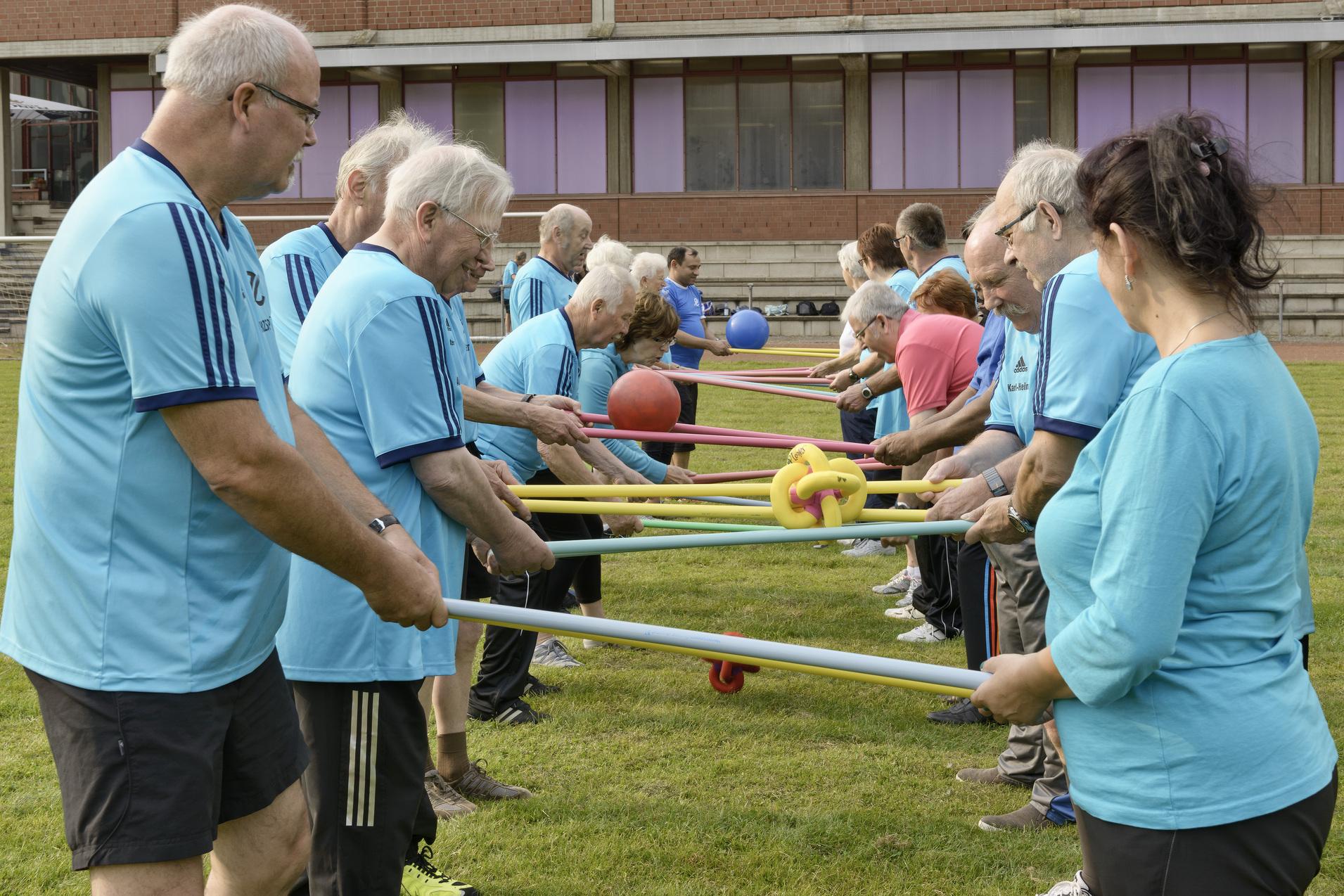 Gruppenevent im Freien: Senioren halten bunte St&auml;be, w&auml;hrend sie an einer Team&uuml;bung teilnehmen.