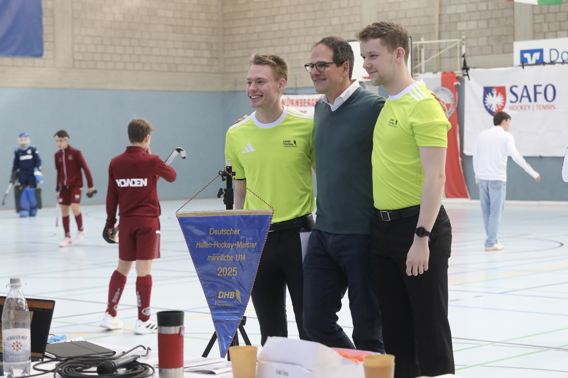 Drei Personen in Sportkleidung stehen l&auml;chelnd vor einem Tisch mit einer Fahne des Deutschen Hockey-Verbandes.