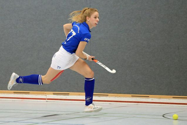 Spielerin in blauer Sportbekleidung sprintet mit dem Hockeyschl&auml;ger in der Hand auf einen kleinen Ball zu.