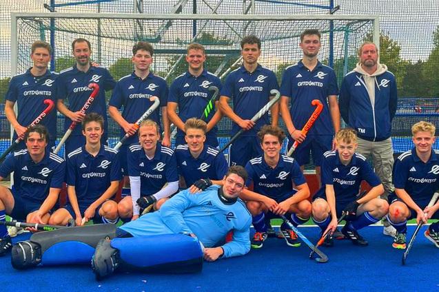 Gruppe von Hockeyspielern in blauen Trikots, um einen Torwart in Ausr&uuml;stung, auf einem Spielfeld posierend.
