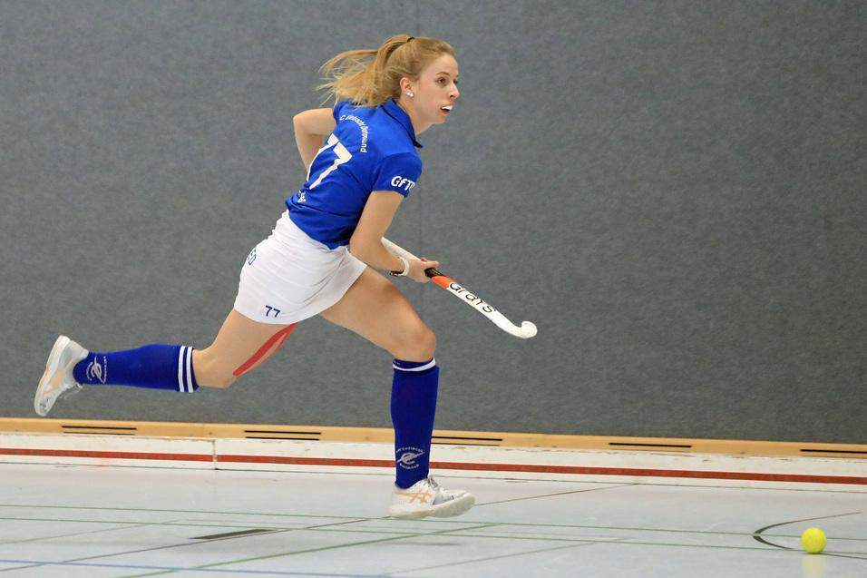 Spielerin in blauer Sportbekleidung sprintet mit dem Hockeyschl&auml;ger in der Hand auf einen kleinen Ball zu.