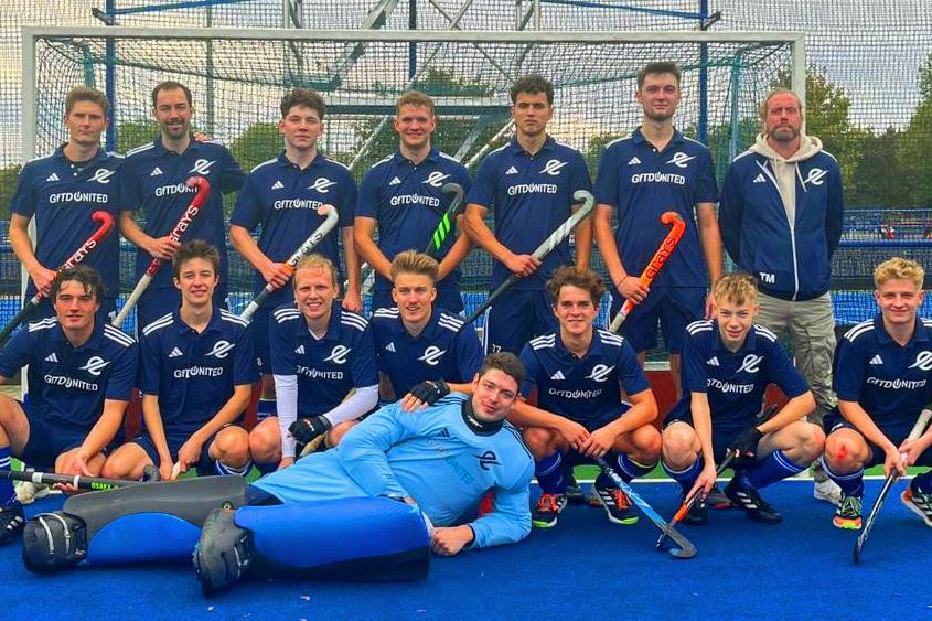 Gruppe von Hockeyspielern in blauen Trikots, um einen Torwart in Ausr&uuml;stung, auf einem Spielfeld posierend.