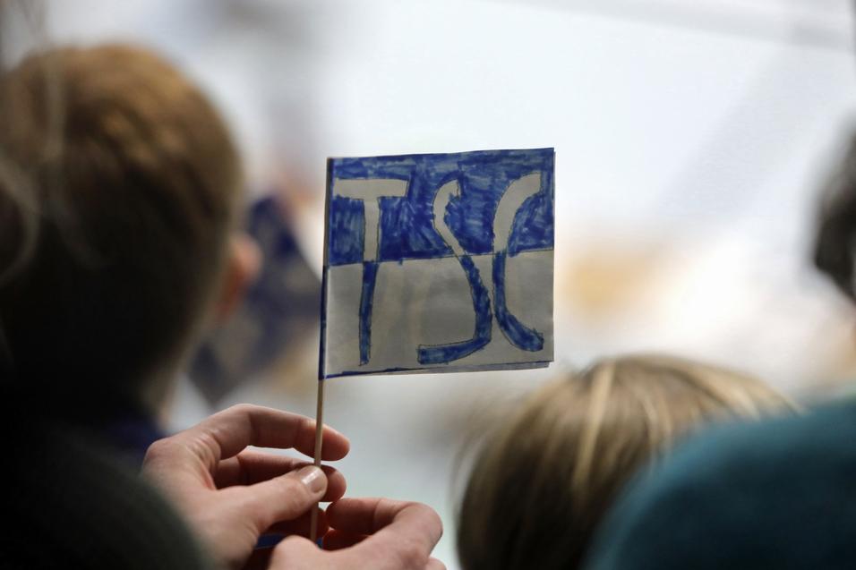 Eine Person h&auml;lt eine kleine, handgemalte Fahne mit der Aufschrift &bdquo;TSC&ldquo; in blauer Schrift vor einer Zuschauergruppe.