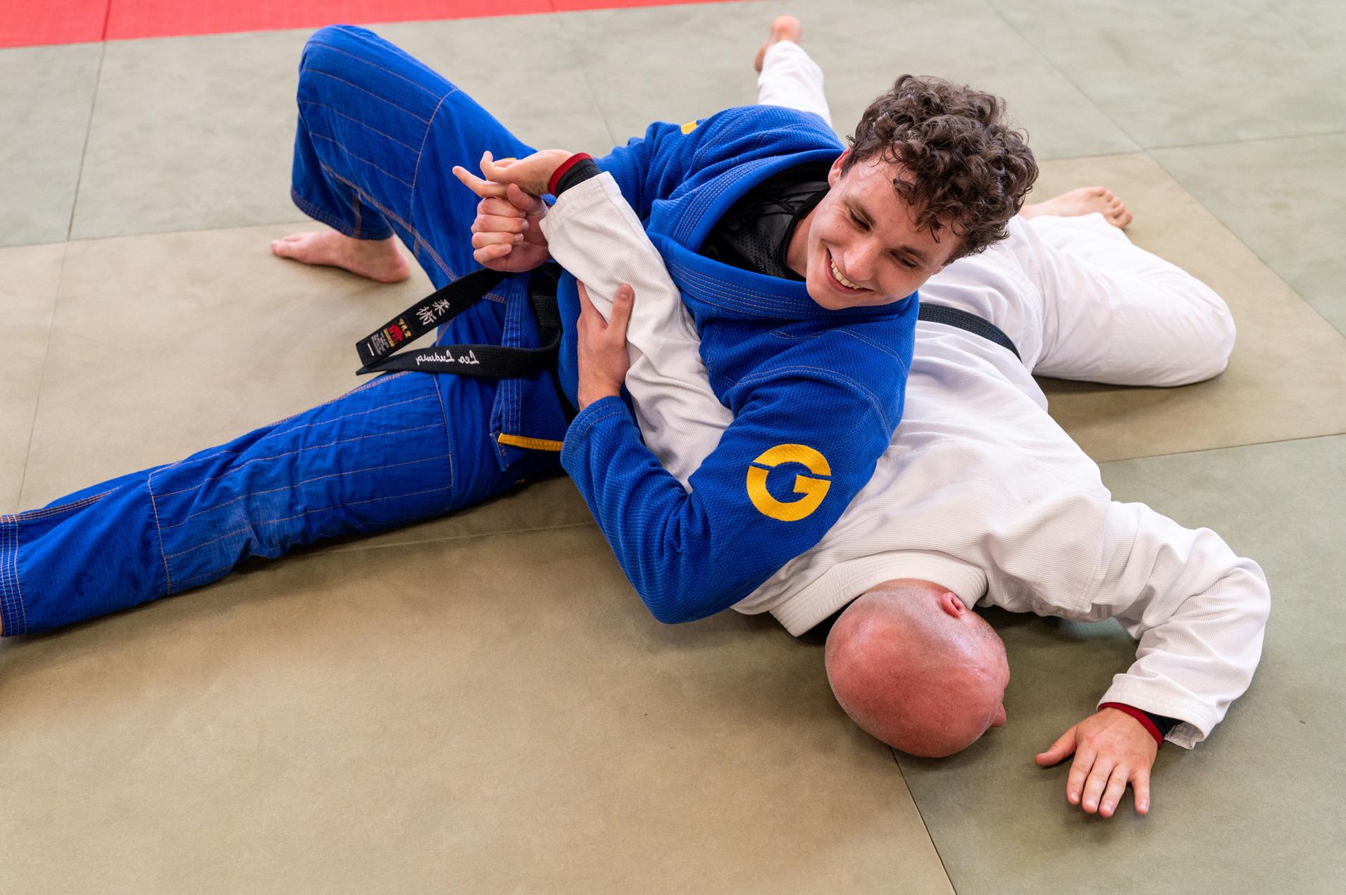 Zwei Judokas im Wettkampf, einer im blauen Gi &uuml;ber dem anderen im wei&szlig;en Gi, der am Boden liegt.