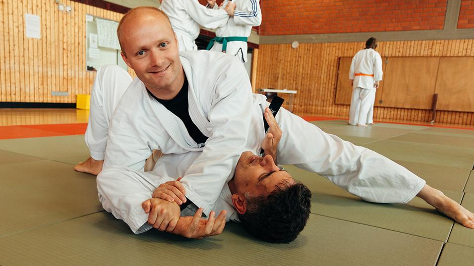 Zwei M&auml;nner in judolike Anz&uuml;gen &uuml;ben in einer Sporthalle einen Halt auf einer Matte.
