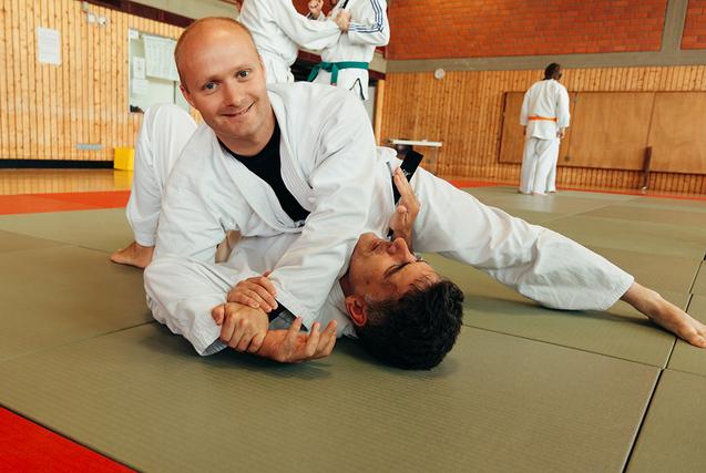 Zwei M&auml;nner in judolike Anz&uuml;gen &uuml;ben in einer Sporthalle einen Halt auf einer Matte.