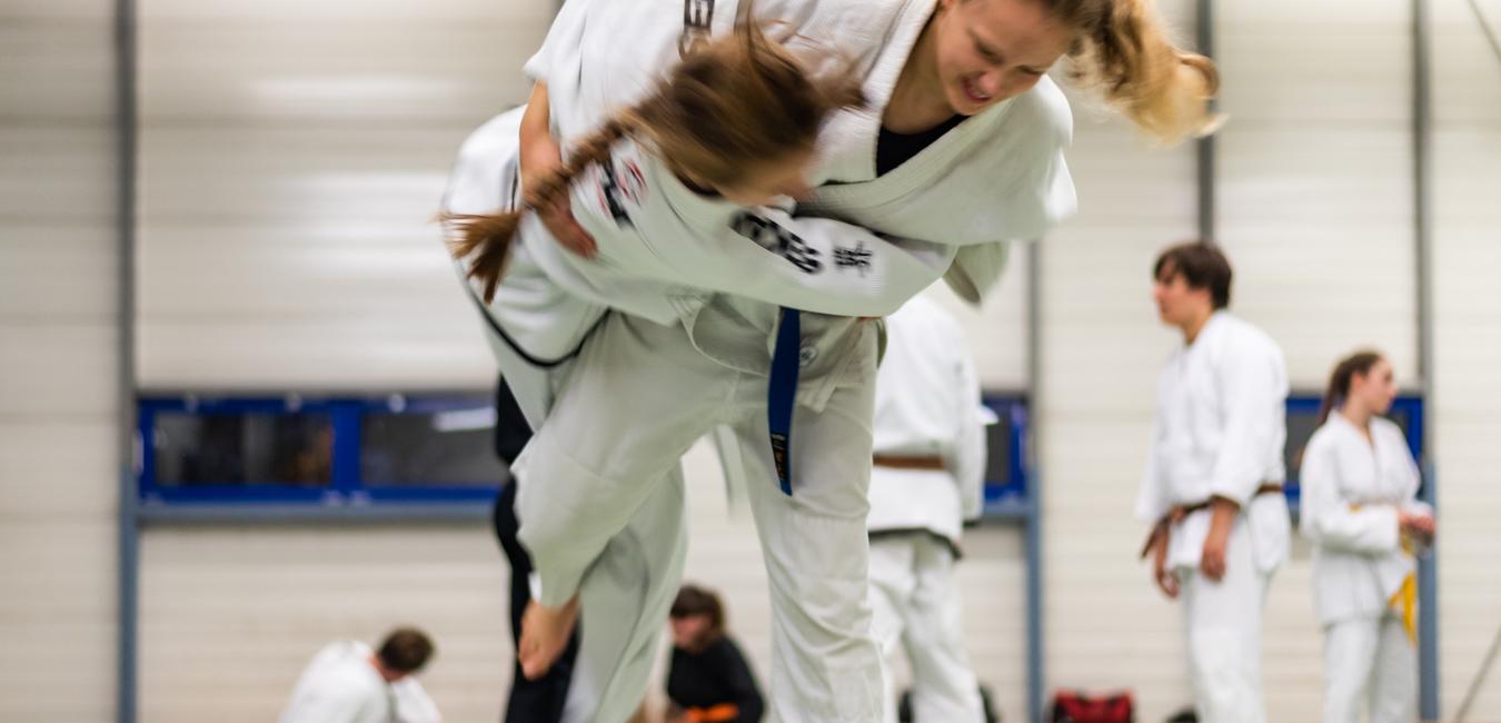 Zwei Judokas im Wettkampf, eine hebt die andere in einer dynamischen Wurfbewegung auf einer Tatami-Matte.