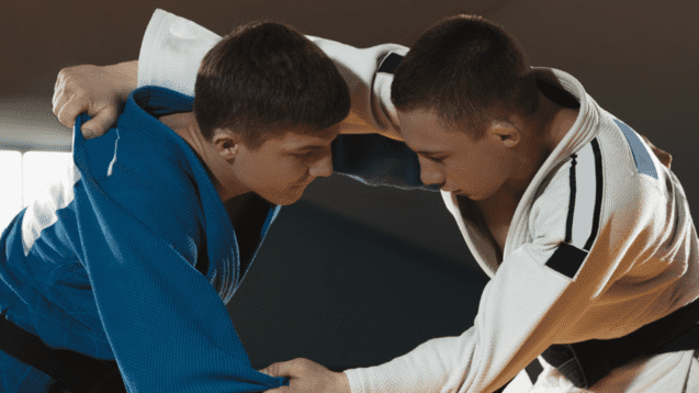 Zwei Judokas im Wettkampf, einer trägt einen blauen und der andere einen weißen Judogi, beide greifen nach den Ärmeln.