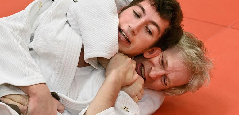 Zwei Judoka im Wettkampf, einer führt einen Würgegriff gegen den anderen auf einer roten Matte aus.