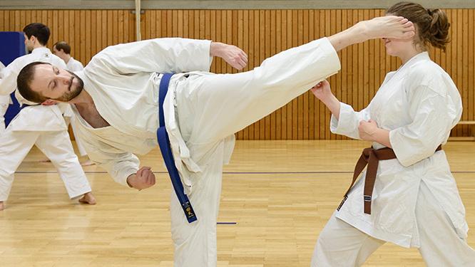 Zwei Karateka in traditioneller Kleidung &uuml;ben Kicks und Techniken in einer Sporthalle w&auml;hrend eines Trainings.