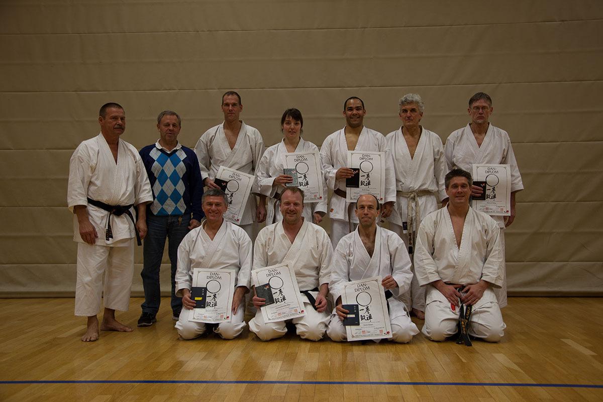 Gruppe von zehn Karateka in Trainingsanz&uuml;gen h&auml;lt Urkunden in einer Sporthalle.