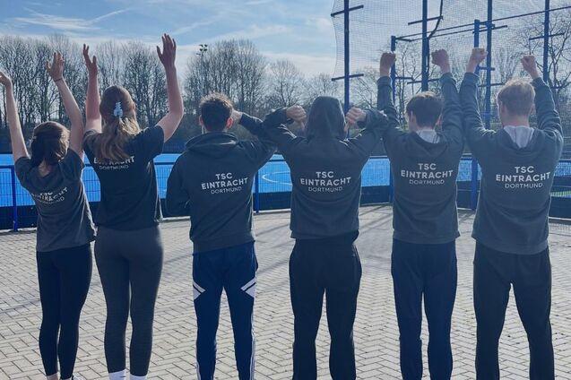 Gruppe von f&uuml;nf Personen in Sweatshirts, die mit erhobenen H&auml;nden auf einem Sportgel&auml;nde stehen. Text: &bdquo;FSJler*innen gesucht!&ldquo;