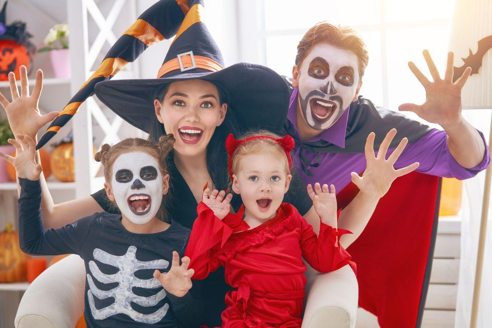 Familie in Halloween-Kost&uuml;men sitzt im Wohnzimmer, &uuml;berzeugt lachend mit gruseligen Gesichtsmasken und Gesten.