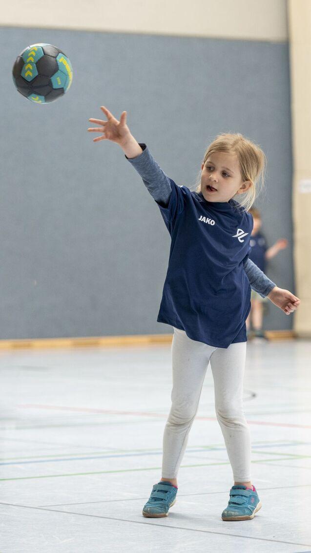 Ein M&auml;dchen wirft einen Handball in einer Sporthalle, tr&auml;gt ein blaues T-Shirt und wei&szlig;e Leggings.